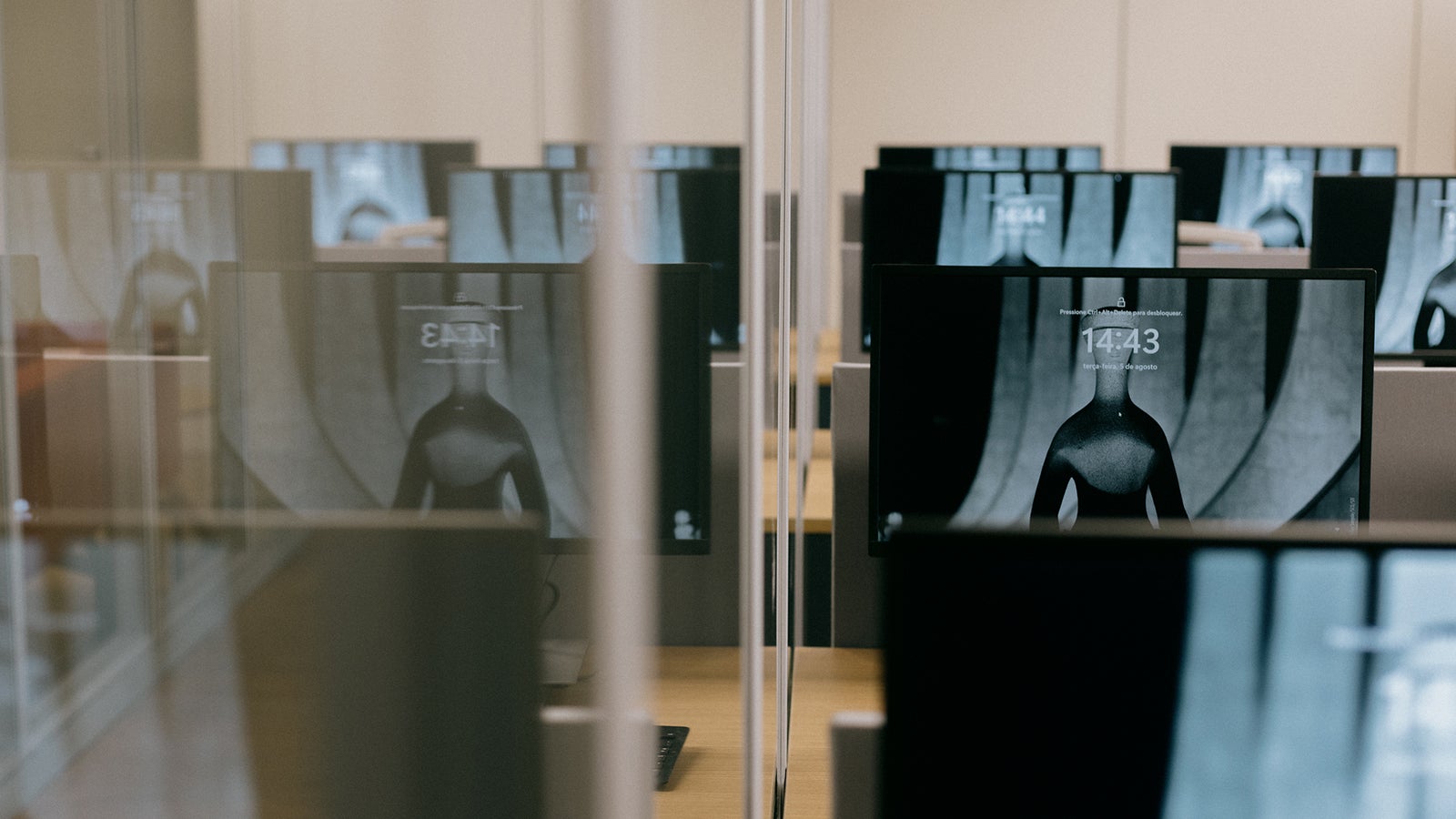 Un espacio de oficina con múltiples monitores de computadora que muestran una imagen similar de un torso, dispuesta en filas y dividida por paneles de vidrio, con el tiempo visiblemente mostrado en las pantallas.